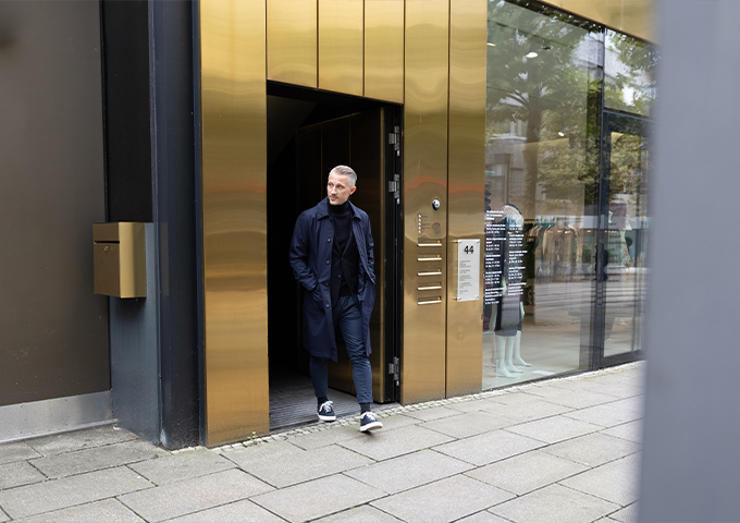 Mann verlässt modernes Bürogebäude mit Glasfassade und goldener Tür.